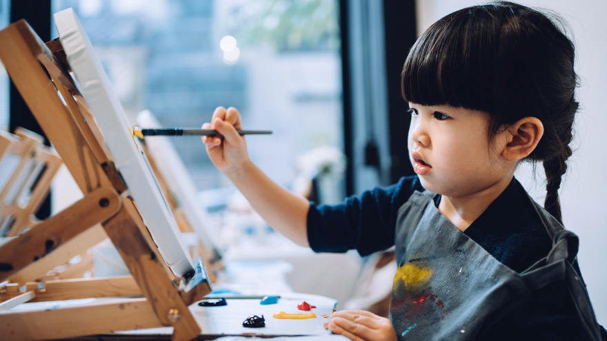 A young girl with dark brown hair painting on a easel