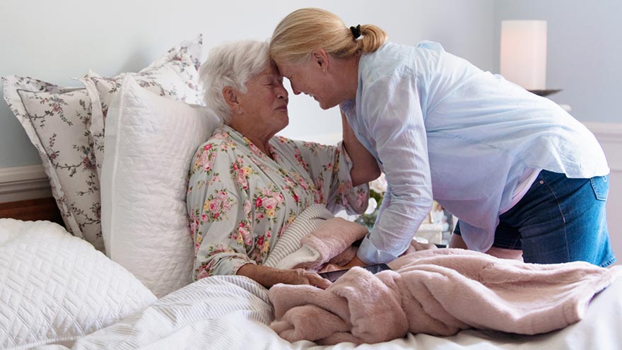 Older lady in bed hugging caregiver or loved one