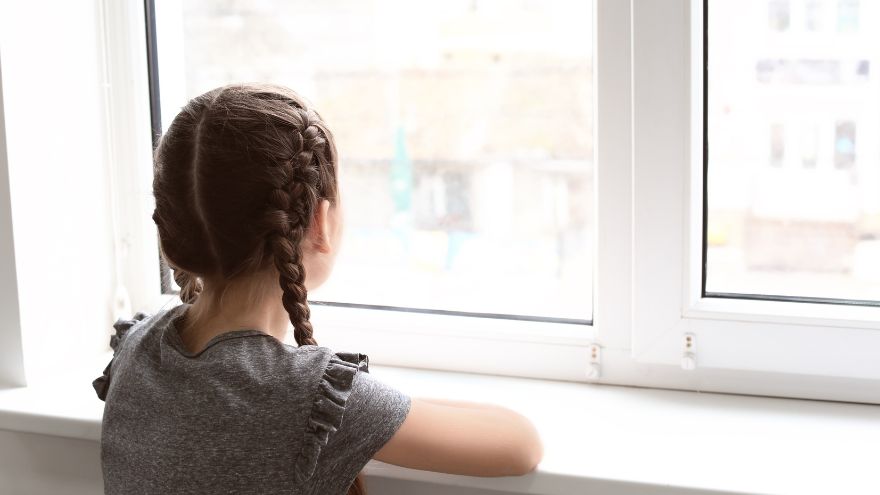 A child stands looking out a raised window