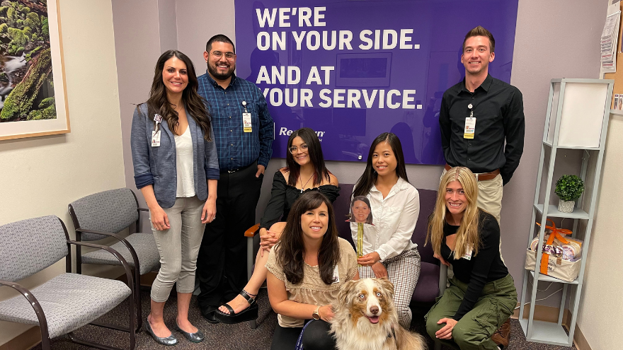 The Patient Experience department at Renown Health pose for a group photo in front of a sign reading, "We're on your side and at your service."