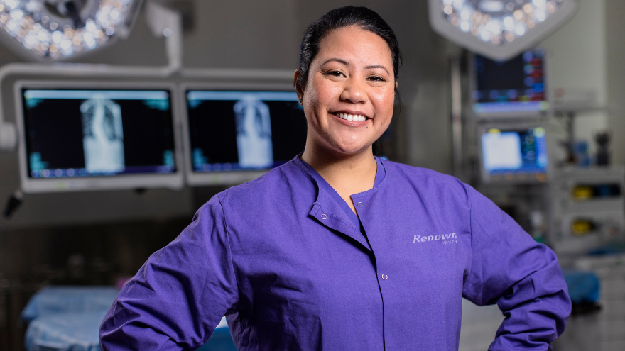 An operating room nurse poses with her hands on her hips in front of operating room equipment.