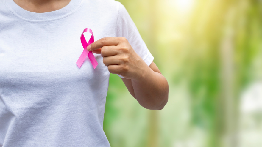 A woman in a while T-shirt holds a pink breast cancer awareness ribbon.