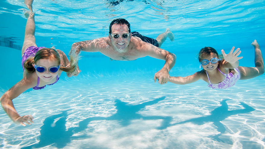 Father swimming underwater with daughters in a pool