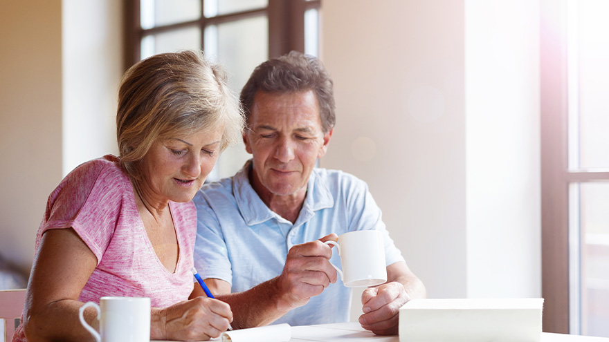 mid-aged couple sitting together with coffee mugs and pen and paper
