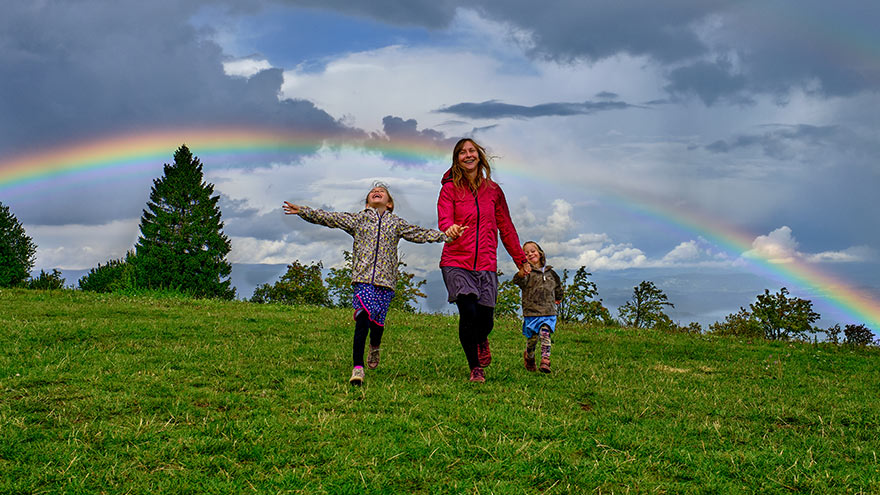 Young mother and her two daughters running downhill with rainbow behind them