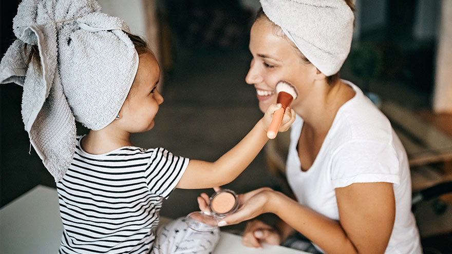  Child applying face powder with brusher to her mother at home