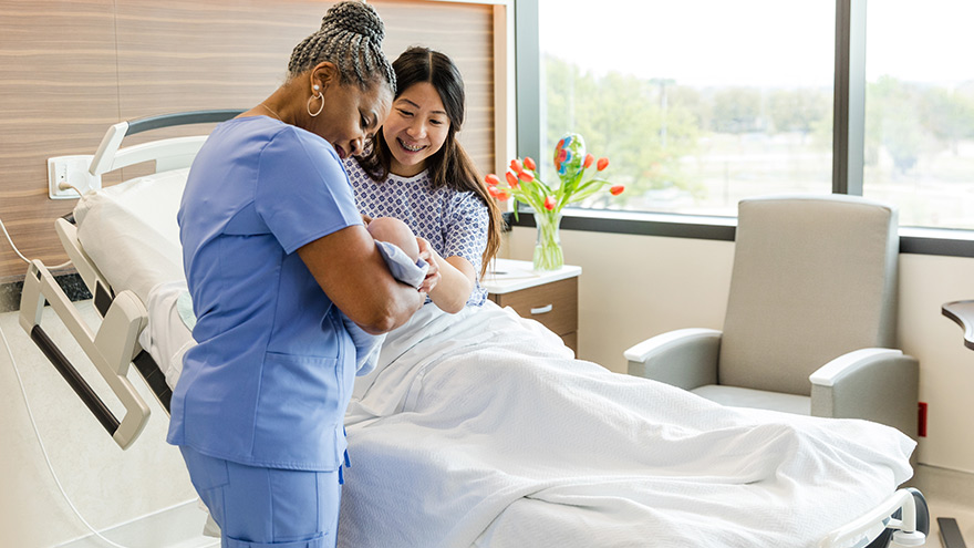 Nurse holding newborn baby while mom looks on